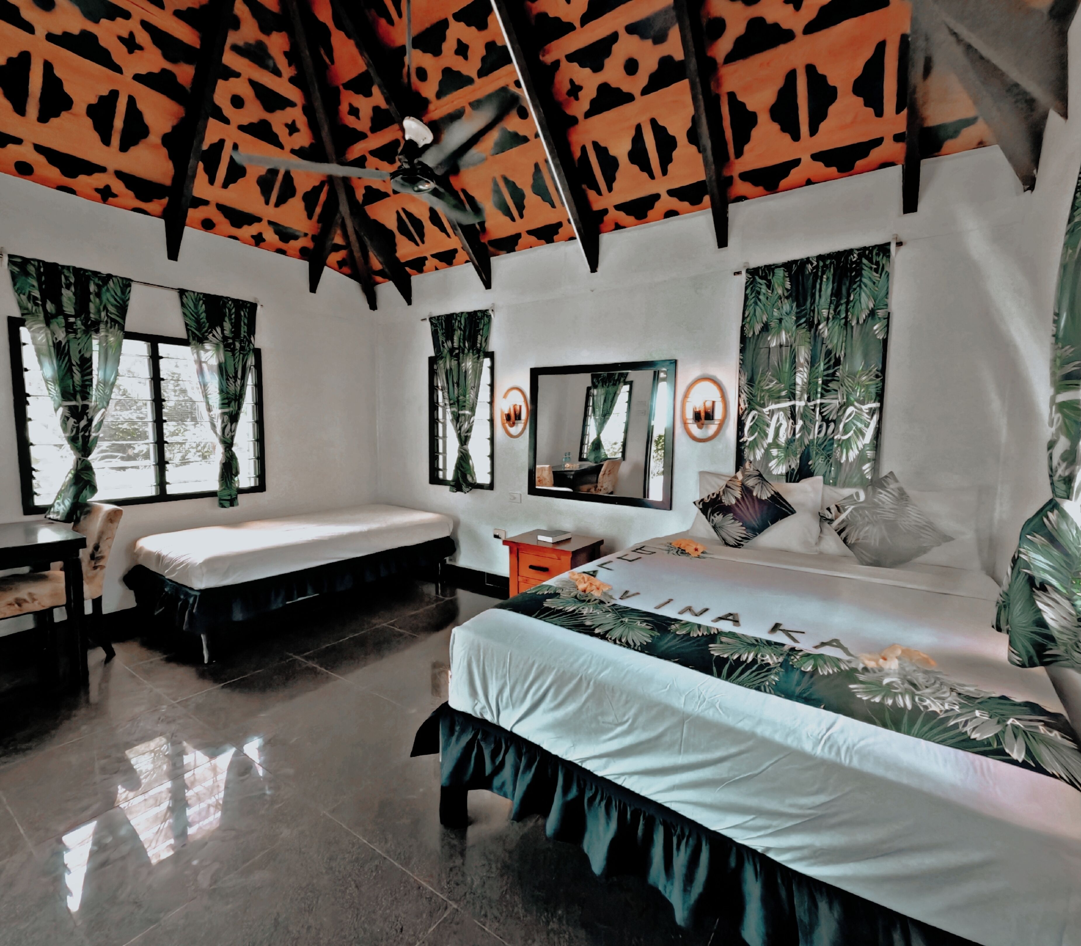 A bedroom with a bed, a desk, a chair, a ceiling fan, and a window with curtains.