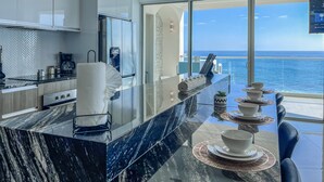 Eine moderne Küche mit Marmorarbeitsplatte, einer Kaffeemaschine und Meerblick.
