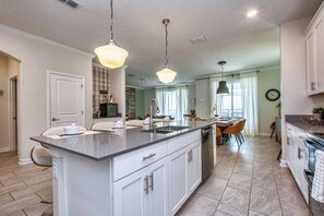 A modern kitchen with a central island, pendant lighting, and a dining area with a view.
