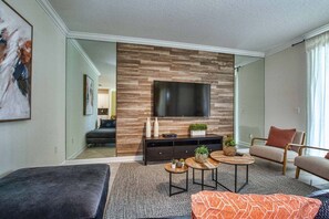 A modern living room with a flat-screen TV, a sofa, a coffee table, and a fireplace.