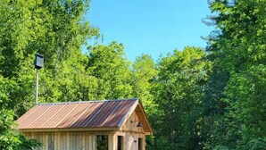 Une cabane en bois rustique, surmontée d’un toit en métal, entourée d’une végétation luxuriante et d’une pelouse bien entretenue.