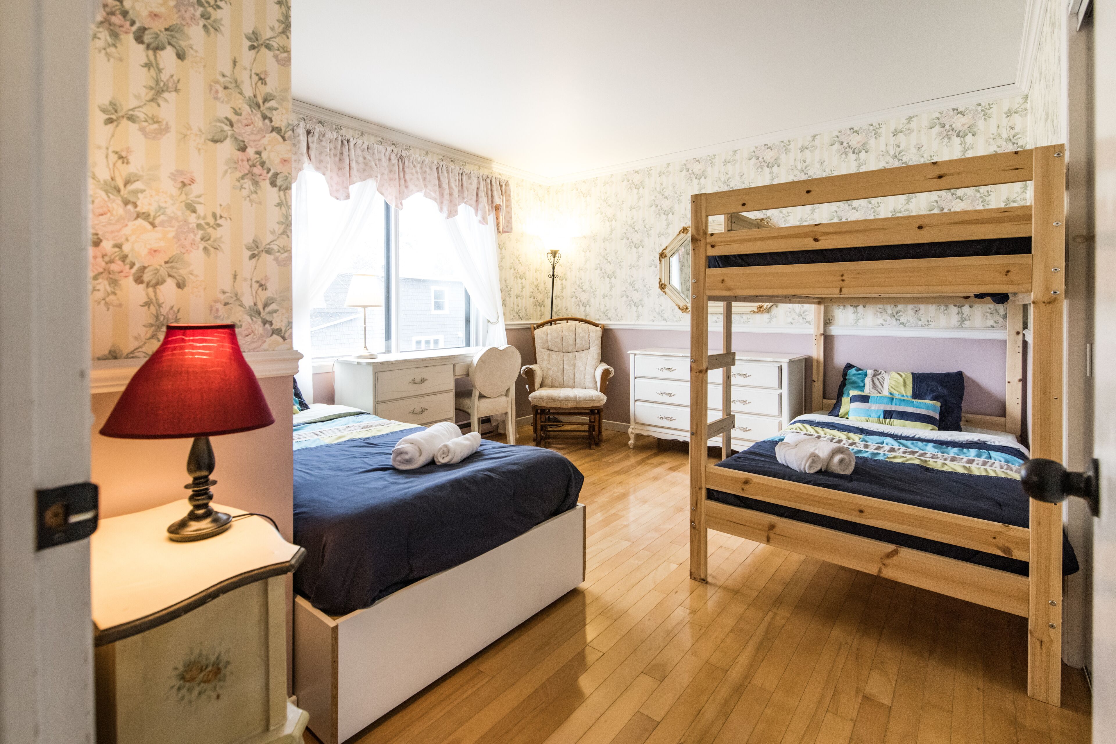 Un dormitorio con una cama doble, una mesita de noche con lámpara, una silla y un aparador.