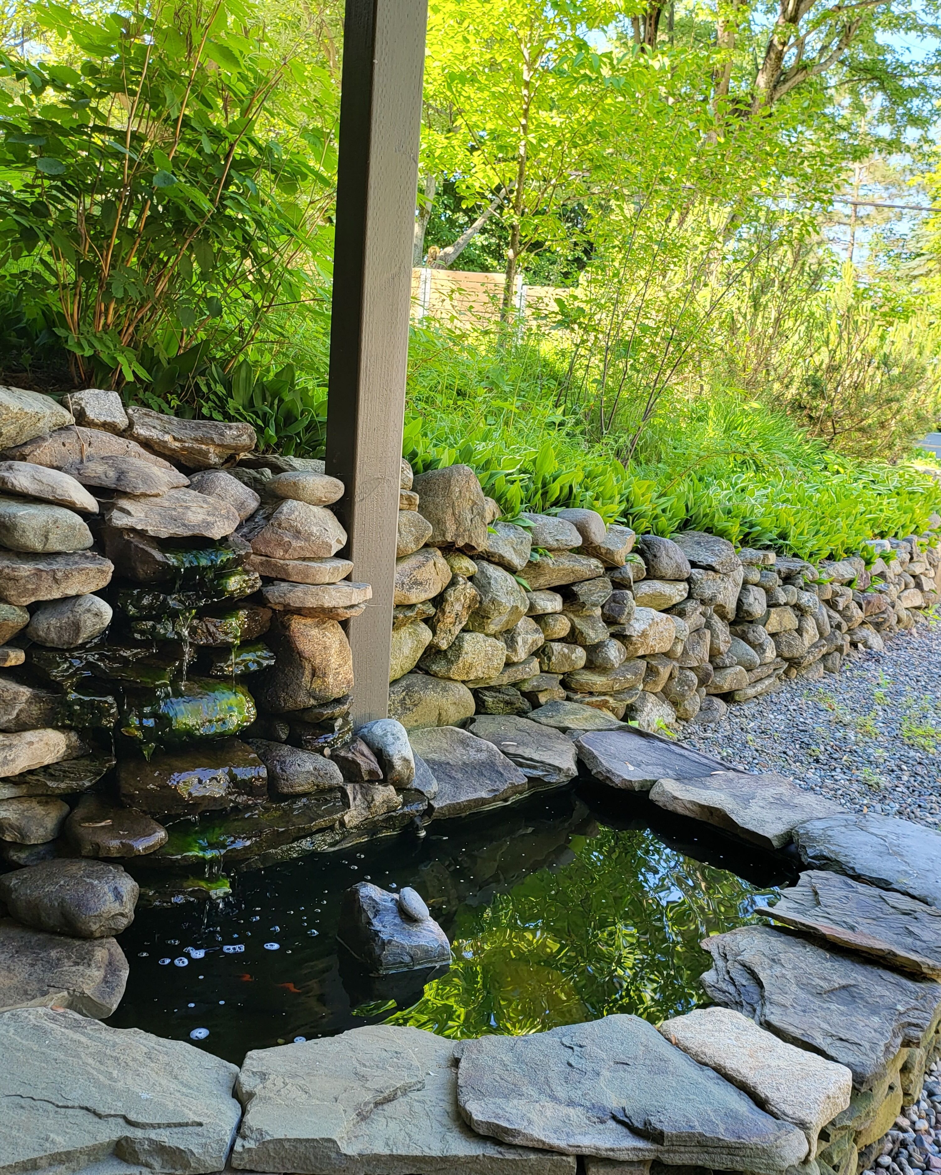 A stone pond with a wooden post, surrounded by a stone wall and lush greenery.