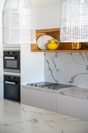 A modern kitchen with a built-in oven, a stove, and a marble backsplash.