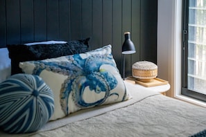 A bedroom with a bed, pillows, a lamp, and a window.