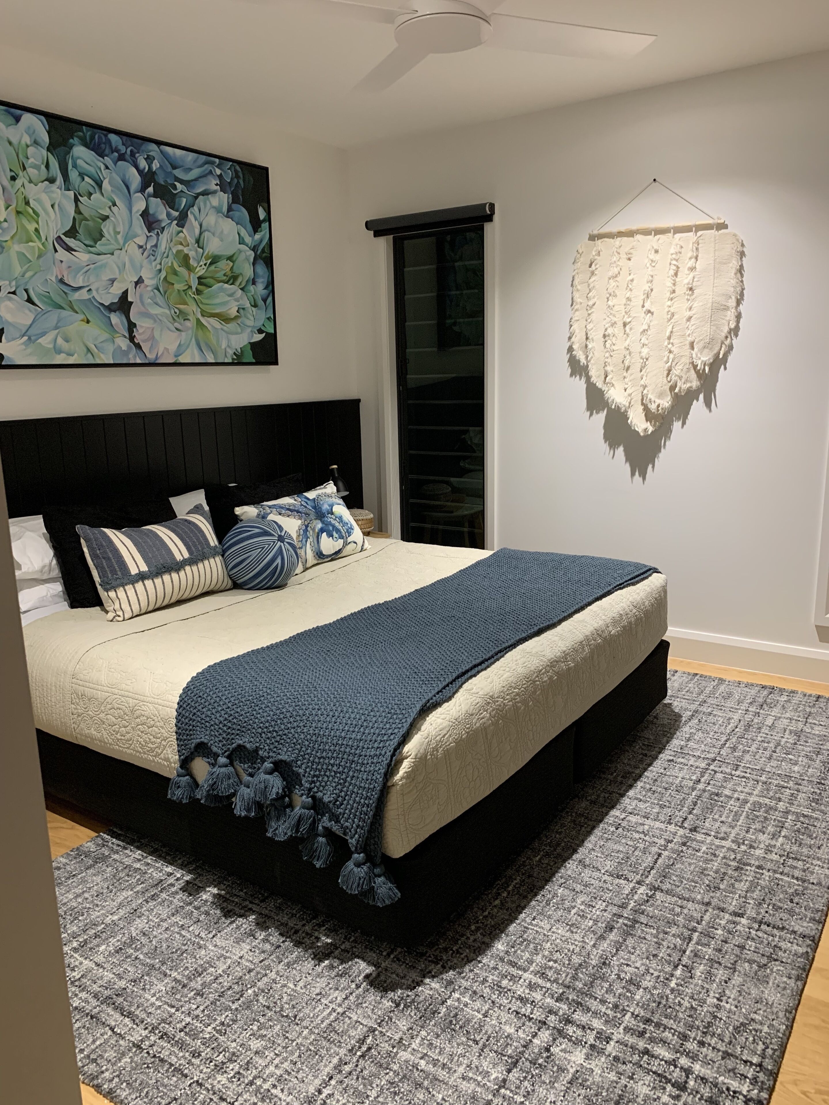 Un dormitorio con una cama, almohadas, una colcha, un cuadro y un tapiz colgante.