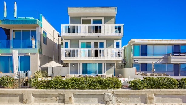 A beachfront hotel with multiple balconies, a pool area, and a sandy beach in the foreground.