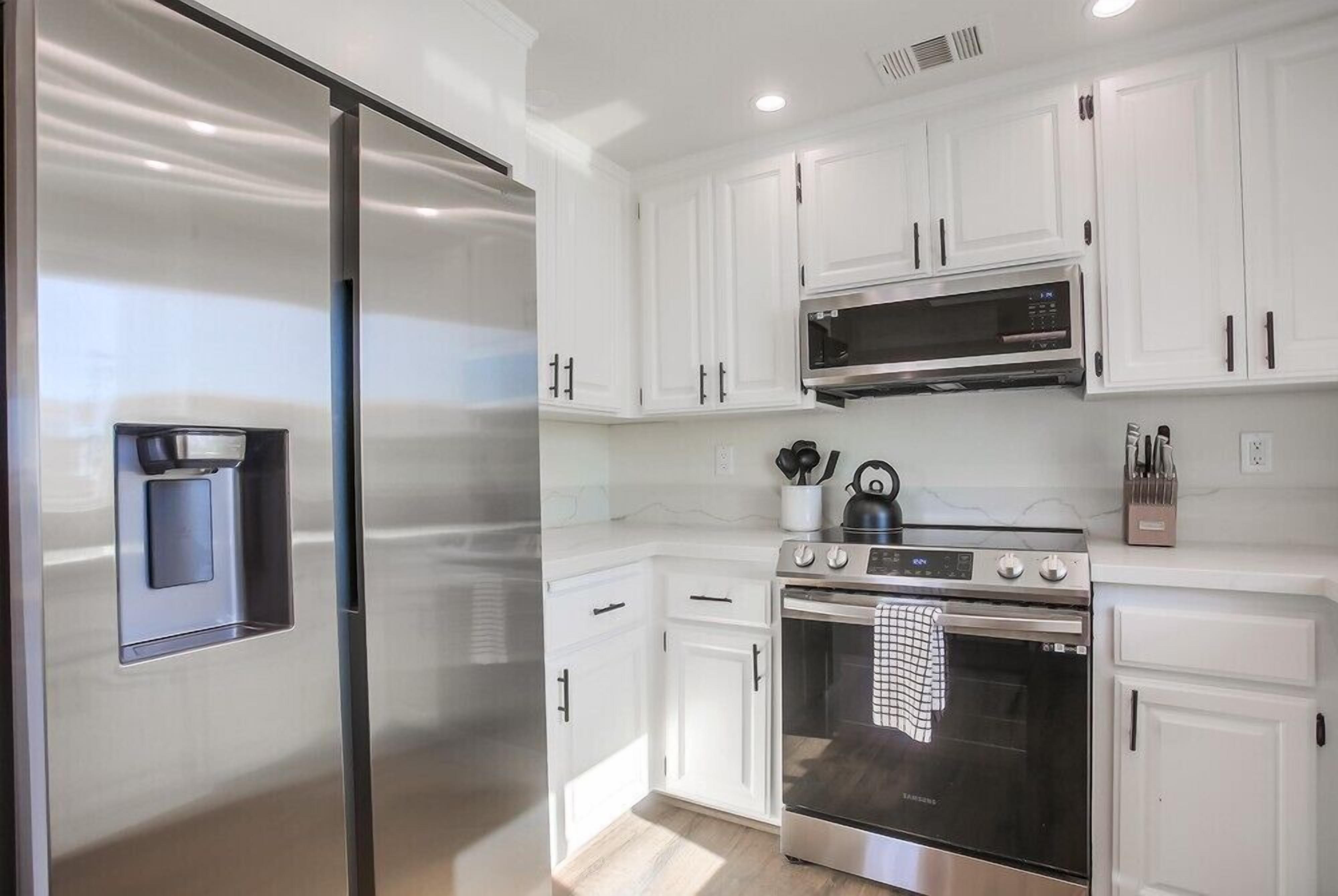 A modern kitchen with white cabinets, a stainless steel refrigerator, a microwave, and a stove.