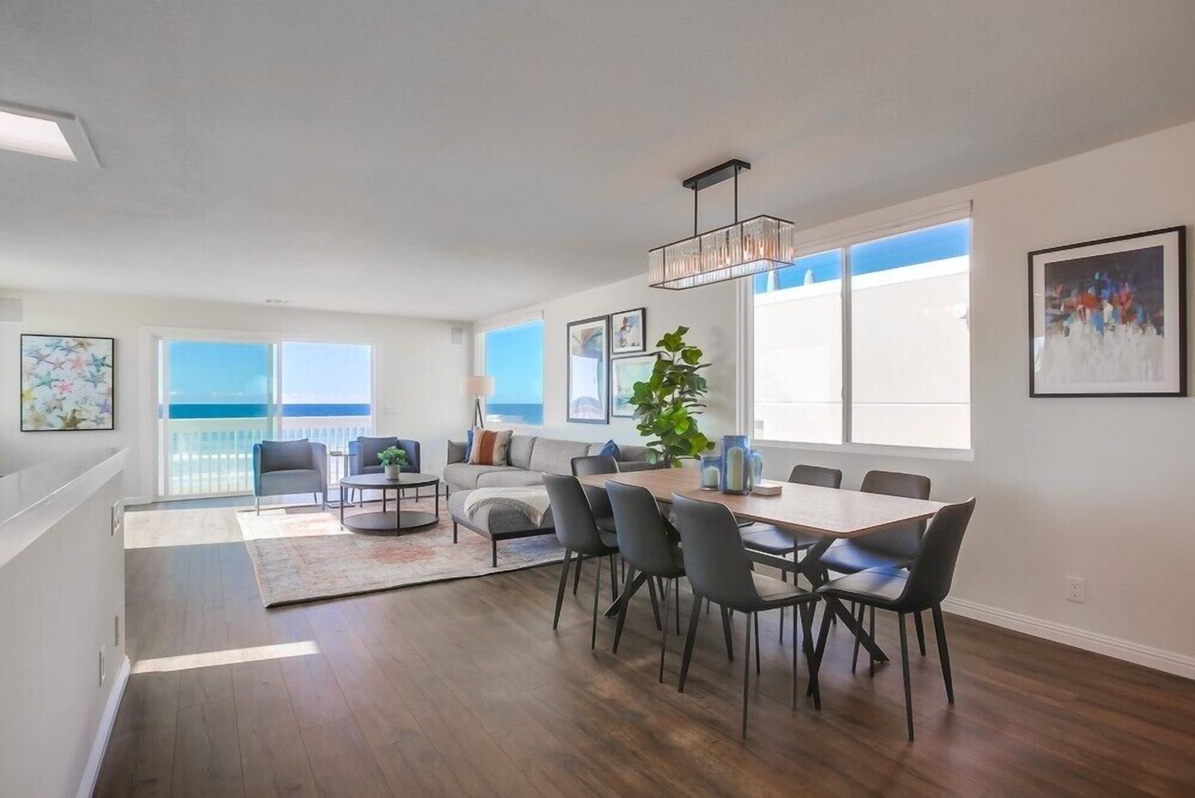 A spacious living area with a dining table and chairs, a sofa, a coffee table, and a large window offering a view of the sky.