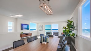 A spacious meeting room with a long wooden table, comfortable seating, a large window with a view, and a modern chandelier.
