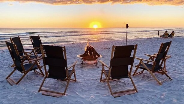 Una playa con un hogar para fogatas y sillas mirando al atardecer.