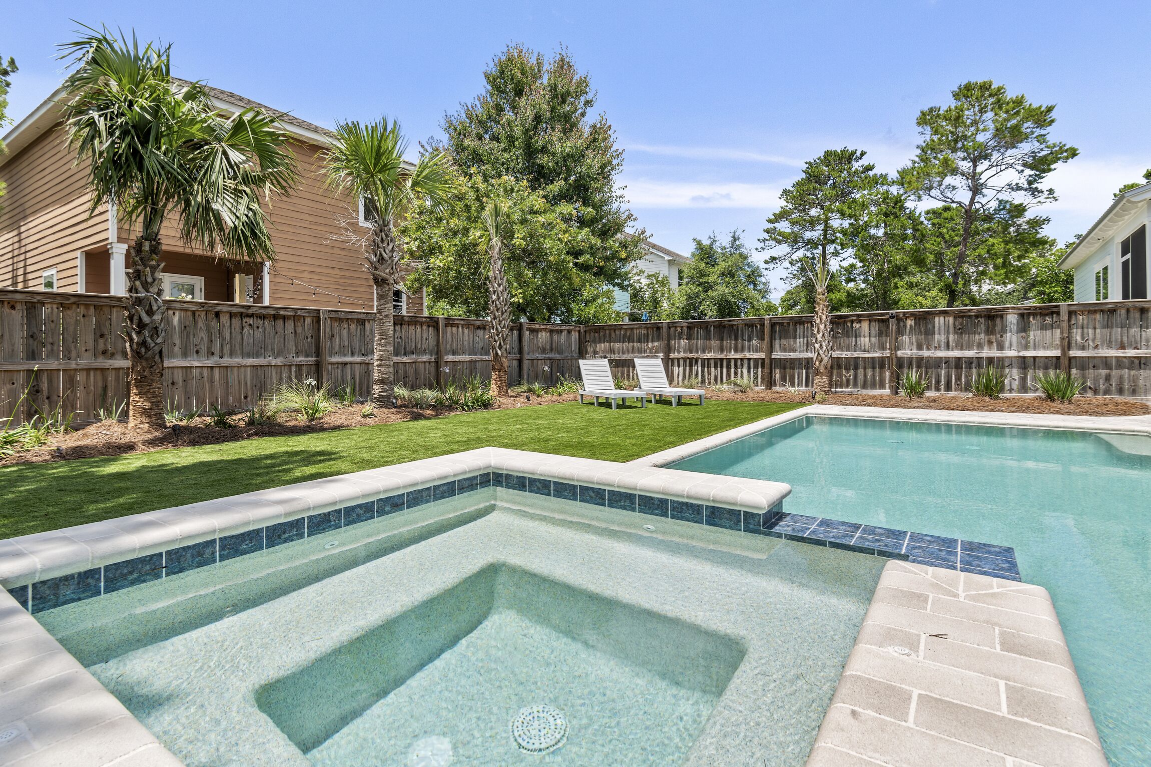 Un jardin avec une piscine, une clôture en bois et une pelouse agrémentée d’un banc.