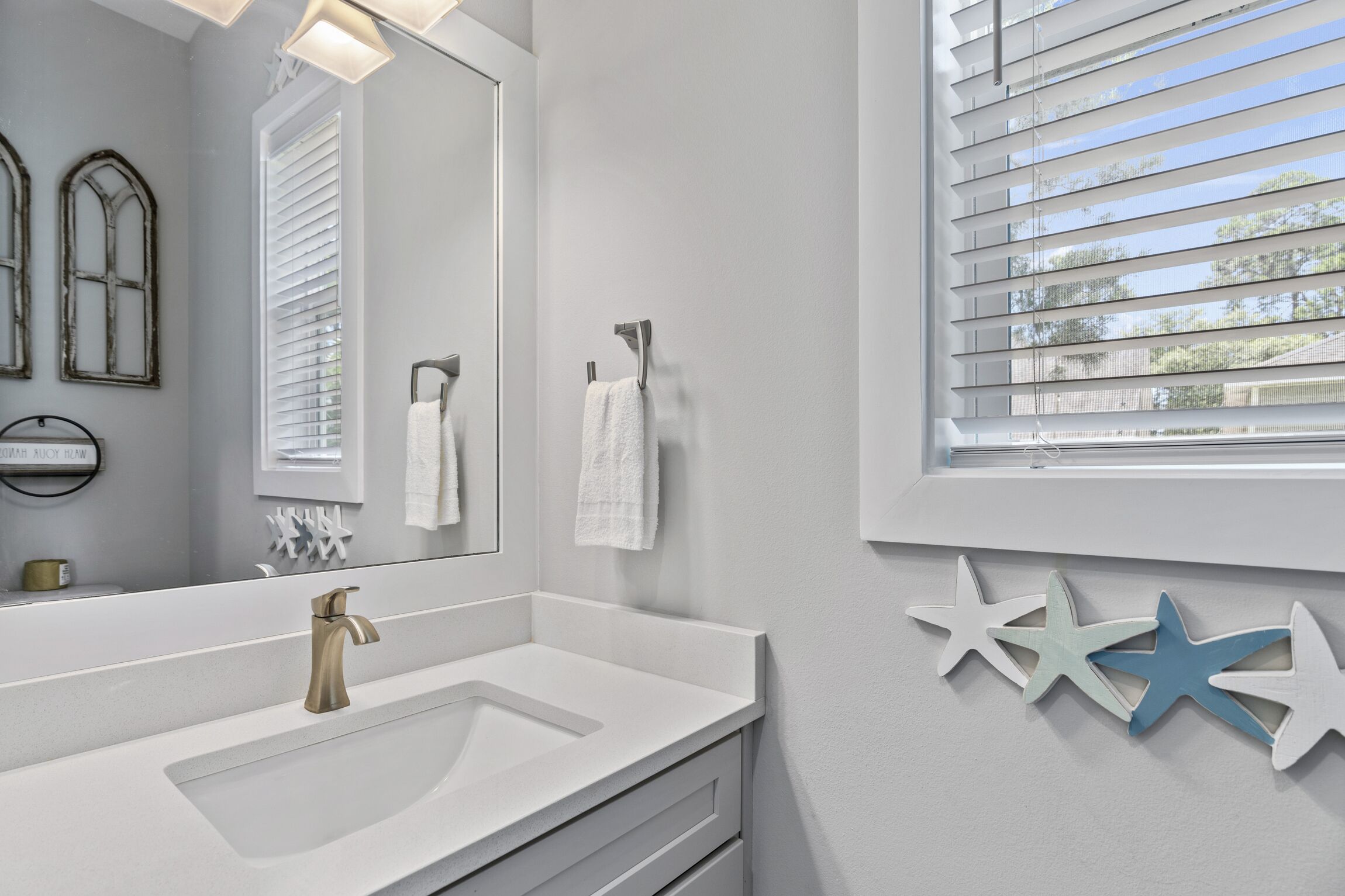 A bathroom with a large mirror, a sink, and a window with blinds.