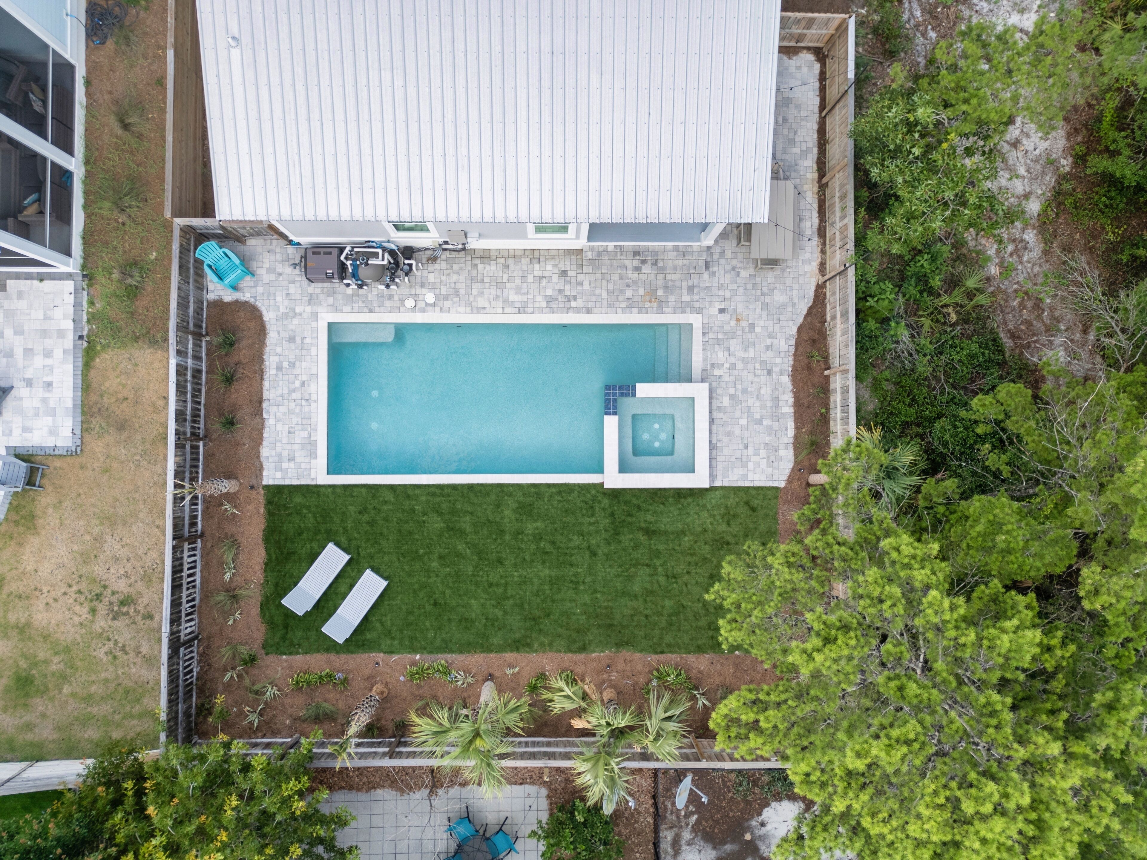 An aerial view of a residential property with a swimming pool, a fenced garden, and a patio area with outdoor furniture.
