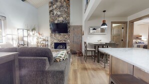Ein modernes Wohnzimmer mit Kamin aus Stein, einem Flachbildfernseher und einem Essbereich mit Holztischen und -stühlen.