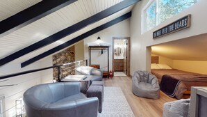 Ein modernes Schlafzimmer im Loft-Stil mit schrägverdeckter Decke, einer Steinwand als Akzent, einem Etagenbett, einem Schreibtisch mit Stuhl und einer gemütlichen Sitzecke.