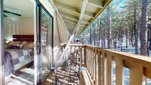 Ein Schlafzimmer mit Bett, Stuhl und Balkon mit Blick auf einen Wald.