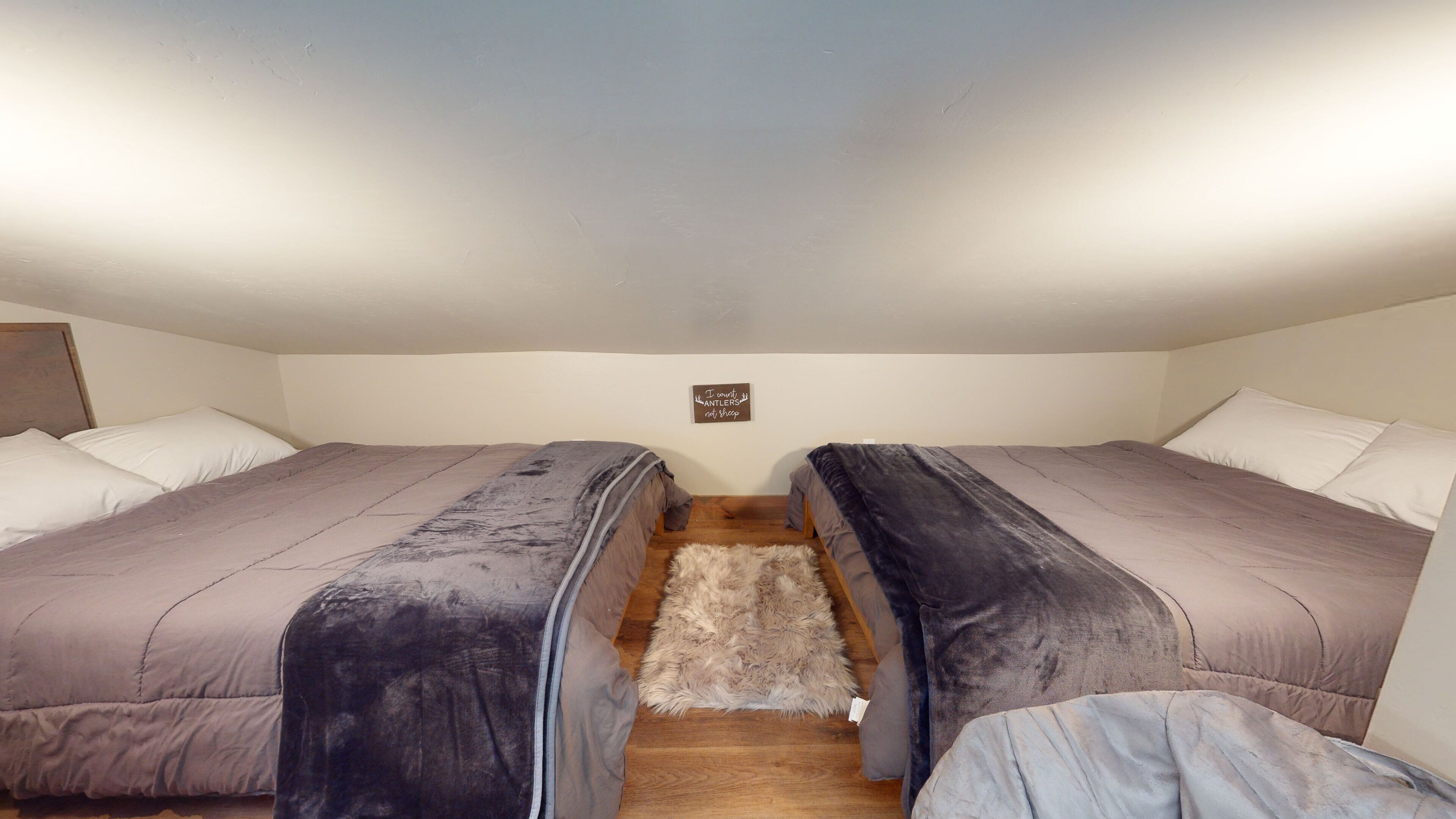 Une petite pièce agréable et chaleureuse, avec deux lits, un plancher en bois et un petit tapis.