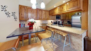 Una cucina moderna con mobili in legno, un piano di lavoro in granito, elettrodomestici in acciaio inossidabile e un'area pranzo con tavolo e sedie.