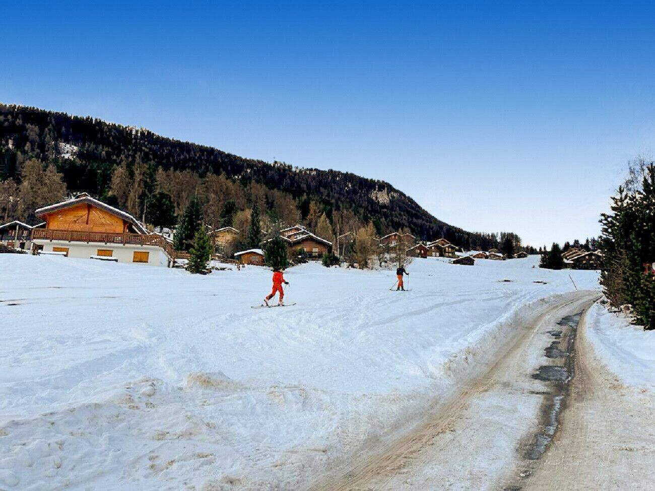 A snow-covered ski resort with wooden chalets and a dirt road.