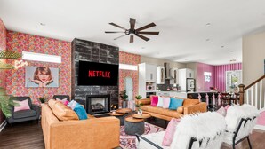 A modern living room with a fireplace, a TV, and a kitchen in the background. - Lipstick n Legends 2 Miles Downtown, Hot Tub, Pool (Nashville)