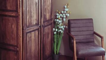 A wooden wardrobe, a potted plant with white flowers, and a brown leather chair.