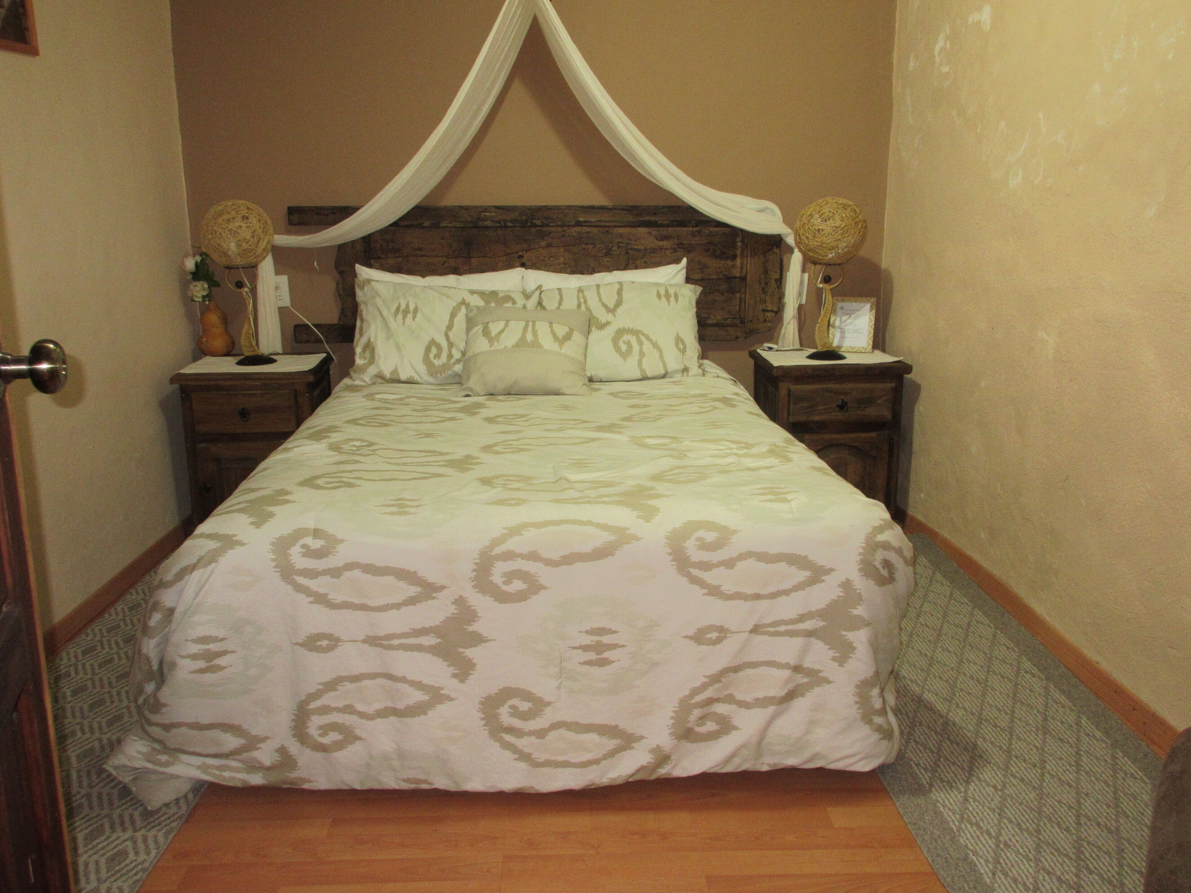 Un dormitorio con cama con dosel, cabecera de madera, mesitas de noche con lámparas y colcha estampada.