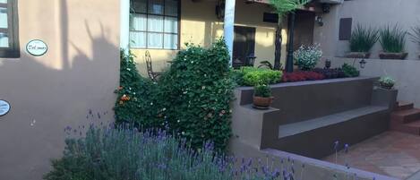 Un patio con una pérgola, plantas en macetas y una variedad de flores.