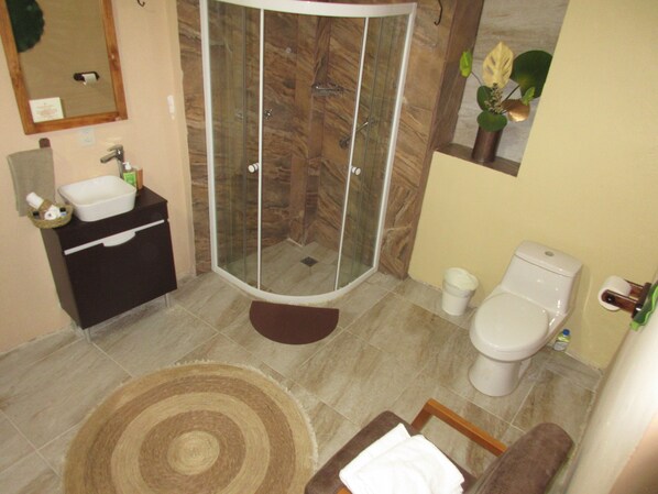 Un baño con ducha de vidrio, lavamanos, inodoro y una pequeña alfombra.