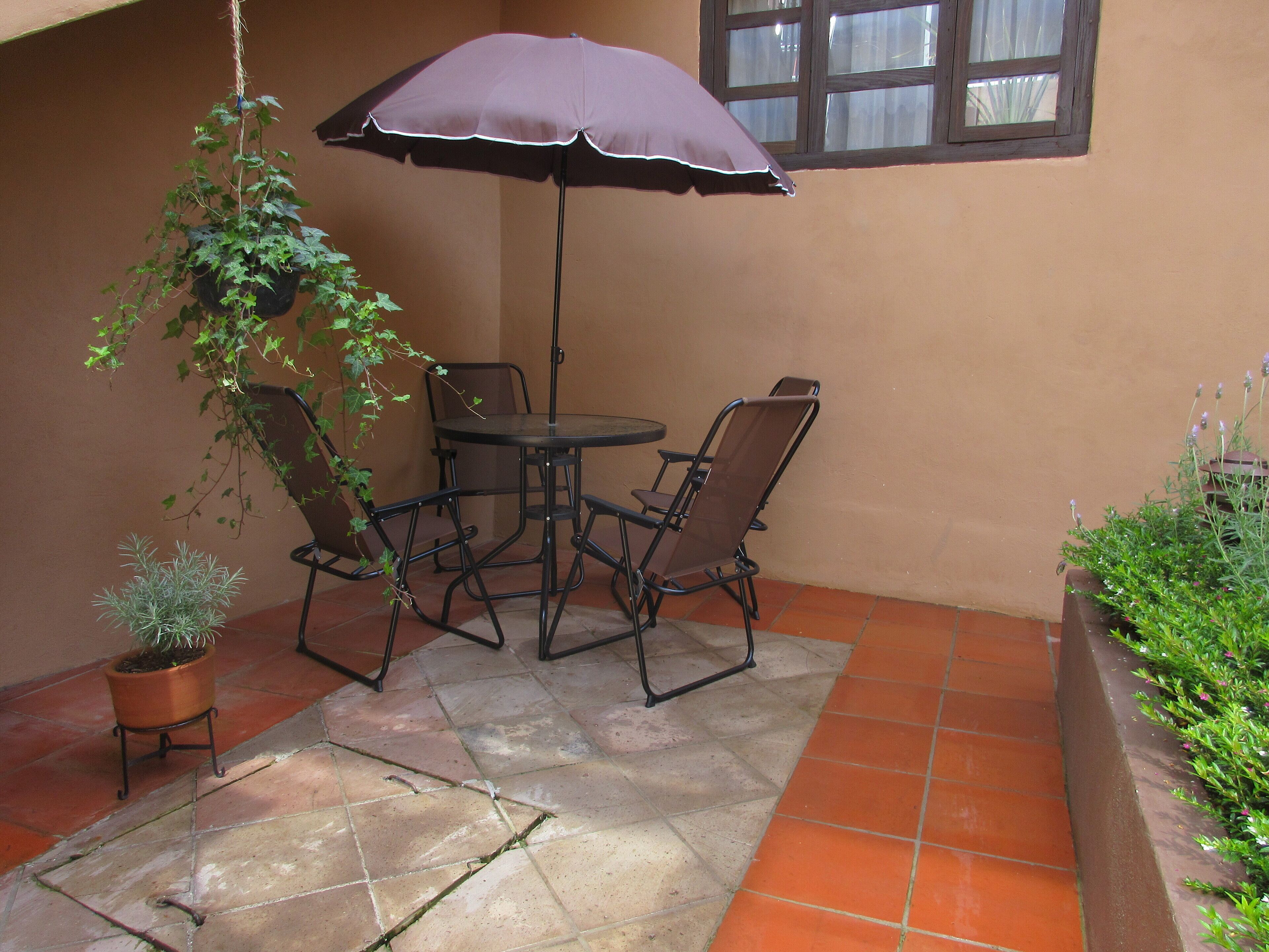 Een terras met een tafel en stoelen, een hangplant en een raam.