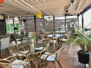 Un patio al aire libre con muebles de mimbre, plantas en macetas y una vista de edificios al fondo.