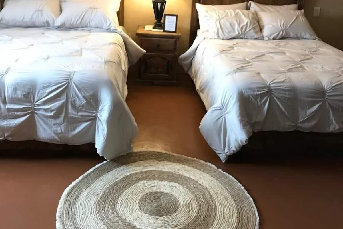 A hotel room with two beds, a round woven rug, and a nightstand with a lamp.