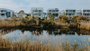 A row of coastal houses with balconies, a calm lake, and surrounding vegetation. - Incredible Water Views on Carolina Beach - The Happy House (Carolina Beach)