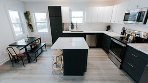 A modern kitchen with white cabinetry, a central island, and a dining area with a bench and chairs. - Incredible Water Views on Carolina Beach - The Happy House (Carolina Beach)