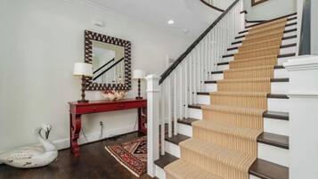 Un escalier recouvert d’une moquette beige, avec des marches en bois foncé, menant à un palier où se trouve une console rouge et un miroir à cadre géométrique.