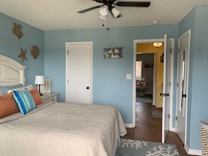 A bedroom with a bed, a ceiling fan, and a door leading to another room.