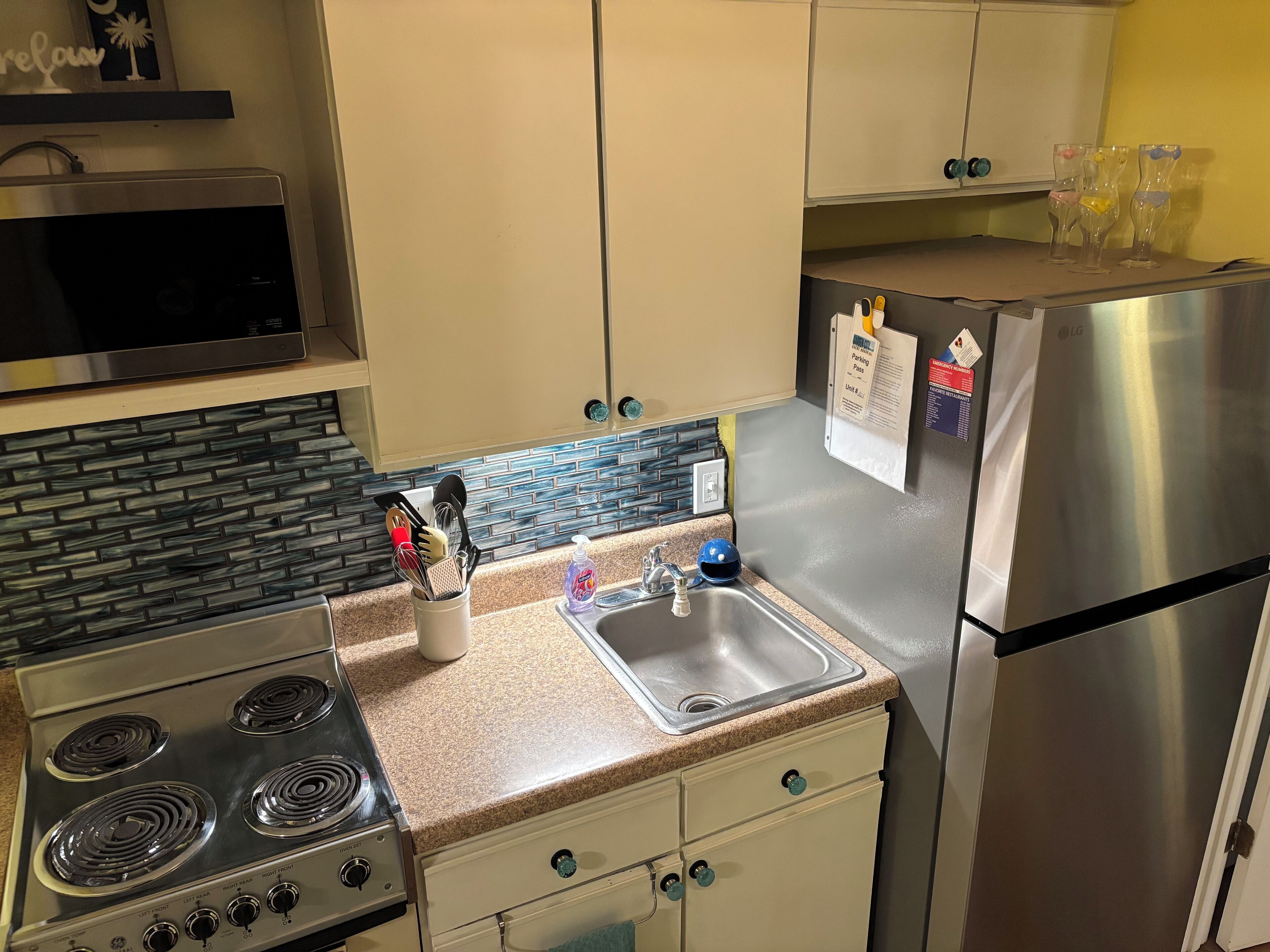 A kitchen with a stainless steel refrigerator, a microwave, a stove, and a sink. There are cabinets, a countertop, and a backsplash.