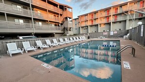 A swimming pool with lounge chairs, a fenced area, and a multi-story building with balconies. - Steps Away From Garden City Pier And Beach! (Murrells Inlet)