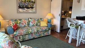 A living room with a sofa, a dining area with a chair, a kitchen in the background, and a sliding door leading to another room. - Steps Away From Garden City Pier And Beach! (Murrells Inlet)