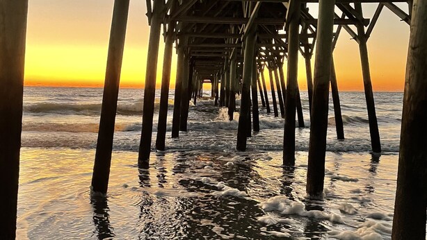 A pier extending into the ocean with waves lapping at its base. - Steps Away From Garden City Pier And Beach! (Murrells Inlet)
