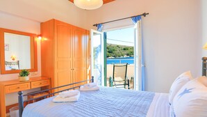 A bedroom with a bed, a wooden wardrobe, a desk with a mirror, and a view of the outdoors.