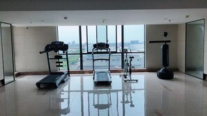 Uma academia espaçosa com esteira, elíptico, bicicleta ergométrica e saco de pancadas, com vista para a cidade através de grandes janelas.