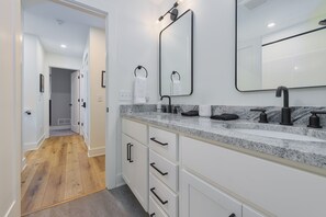 A modern bathroom with a granite countertop, a large mirror, and a walk-in shower.