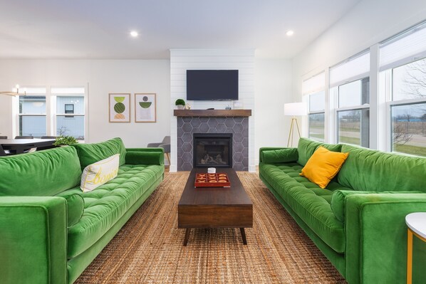 A living room with two green sofas, a wooden coffee table, a fireplace, and a large window.