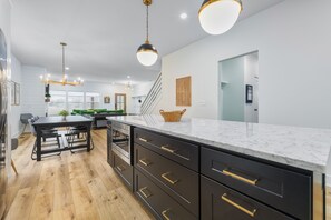 Cozinha moderna com armários pretos, bancadas de mármore e iluminação pendente.