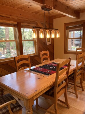 Una mesa de madera para comedor con seis sillas, una lámpara colgante y vistas al exterior a través de amplios ventanales.