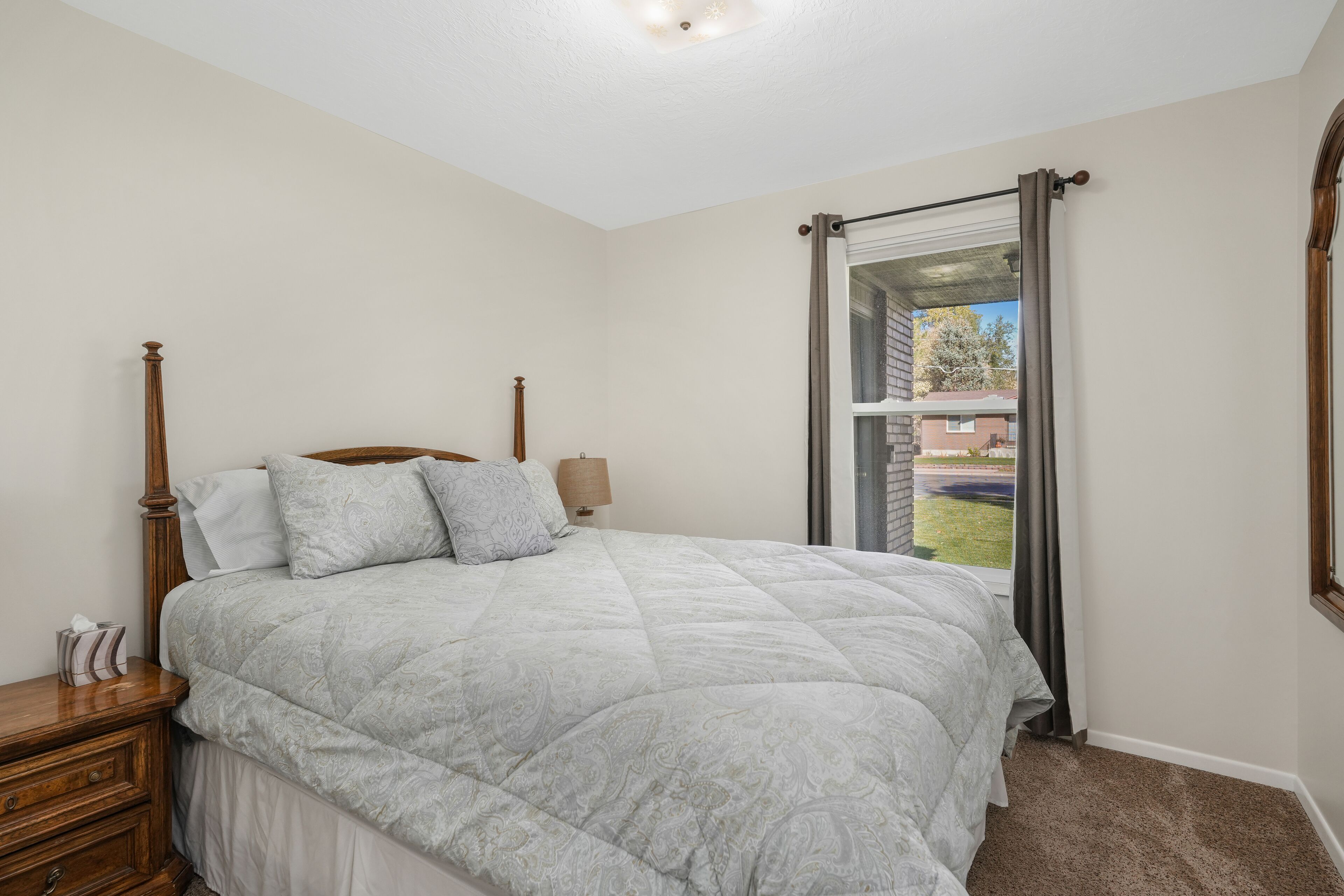 A bedroom with a bed, nightstand, lamp, and a window with curtains.
