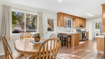 A modern kitchen with wooden cabinets, a central island, and a dining area with a wooden table and chairs.