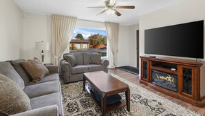 Una sala de estar con sofá, sillón, mesa de centro, mueble de televisión con televisor de pantalla plana y chimenea.