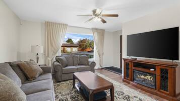 A living room with a sofa, armchair, coffee table, TV stand with a flat-screen TV, and a fireplace.